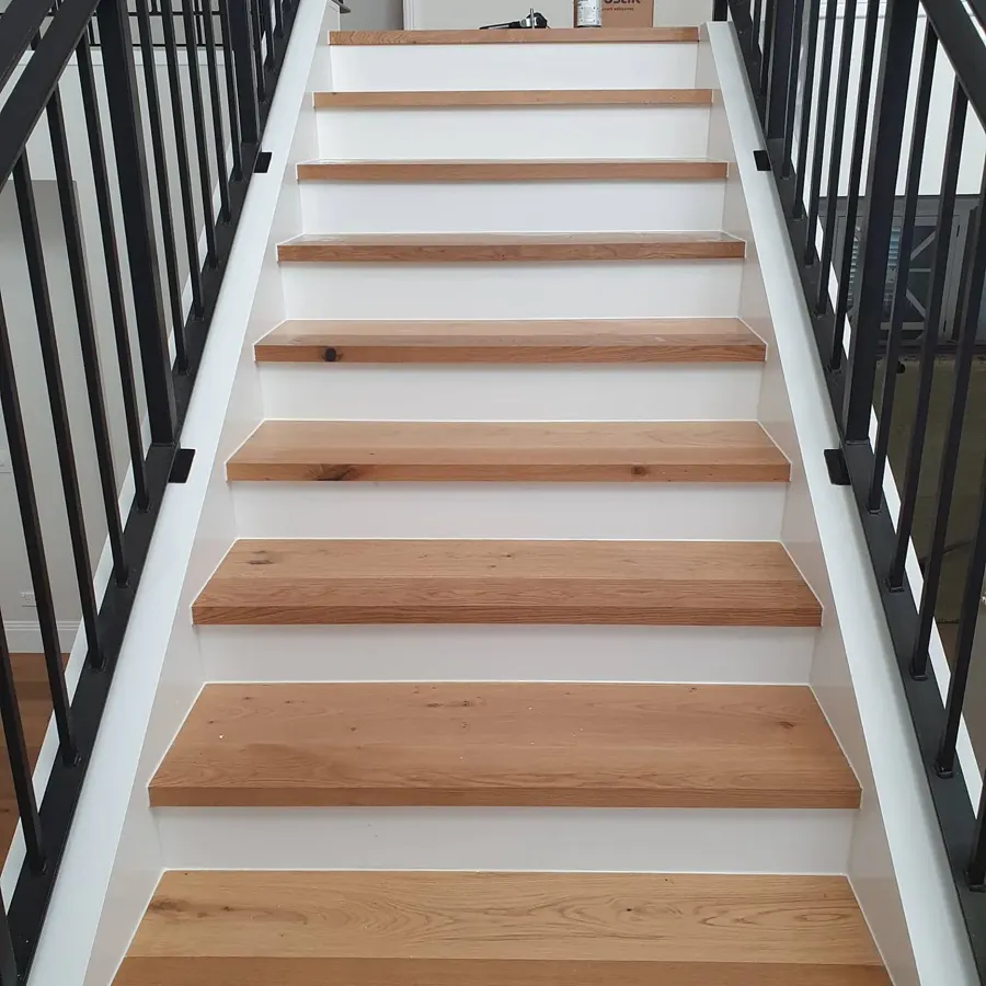 Timber stair treads on white risers, with fine white sealant lines along each junction with the stringer