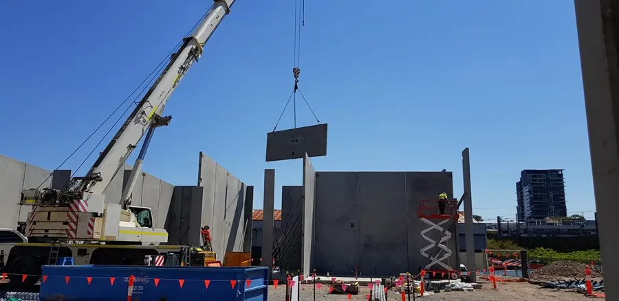 A crane lifting a precast concrete panel into place on a commercial building site
